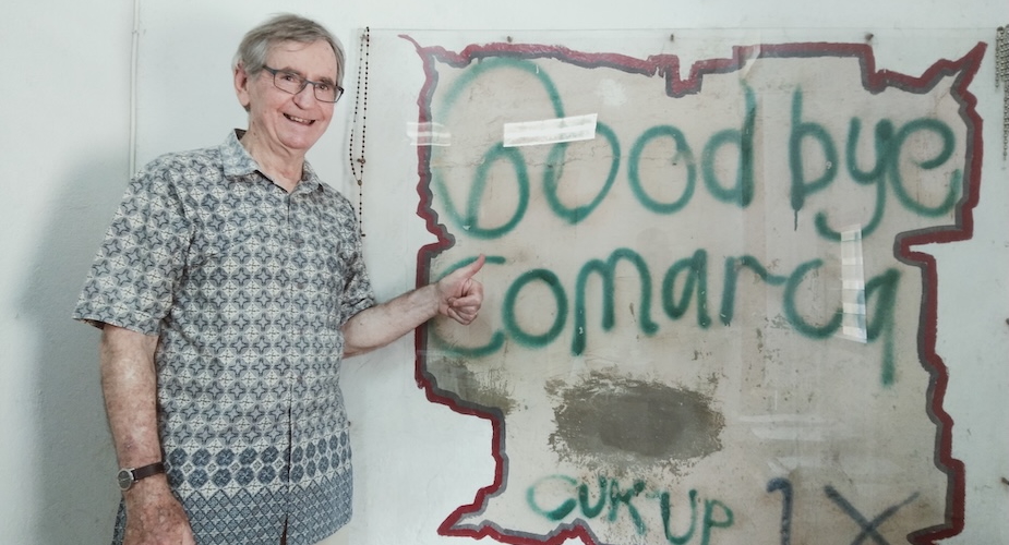 Pat standing beside graffiti done by a political prisoner at Comarca Balide, which was recovered and preserved as part of the building rehabilitation process, Dili, Timor-Leste (late 2000s)/ Pat Walsh archive